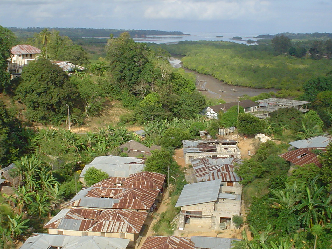 A view over Pemba Island from high ground at Chake Chake: tin-roofed houses among dense green vegetation, with a tidal creek and mangroves beyond.