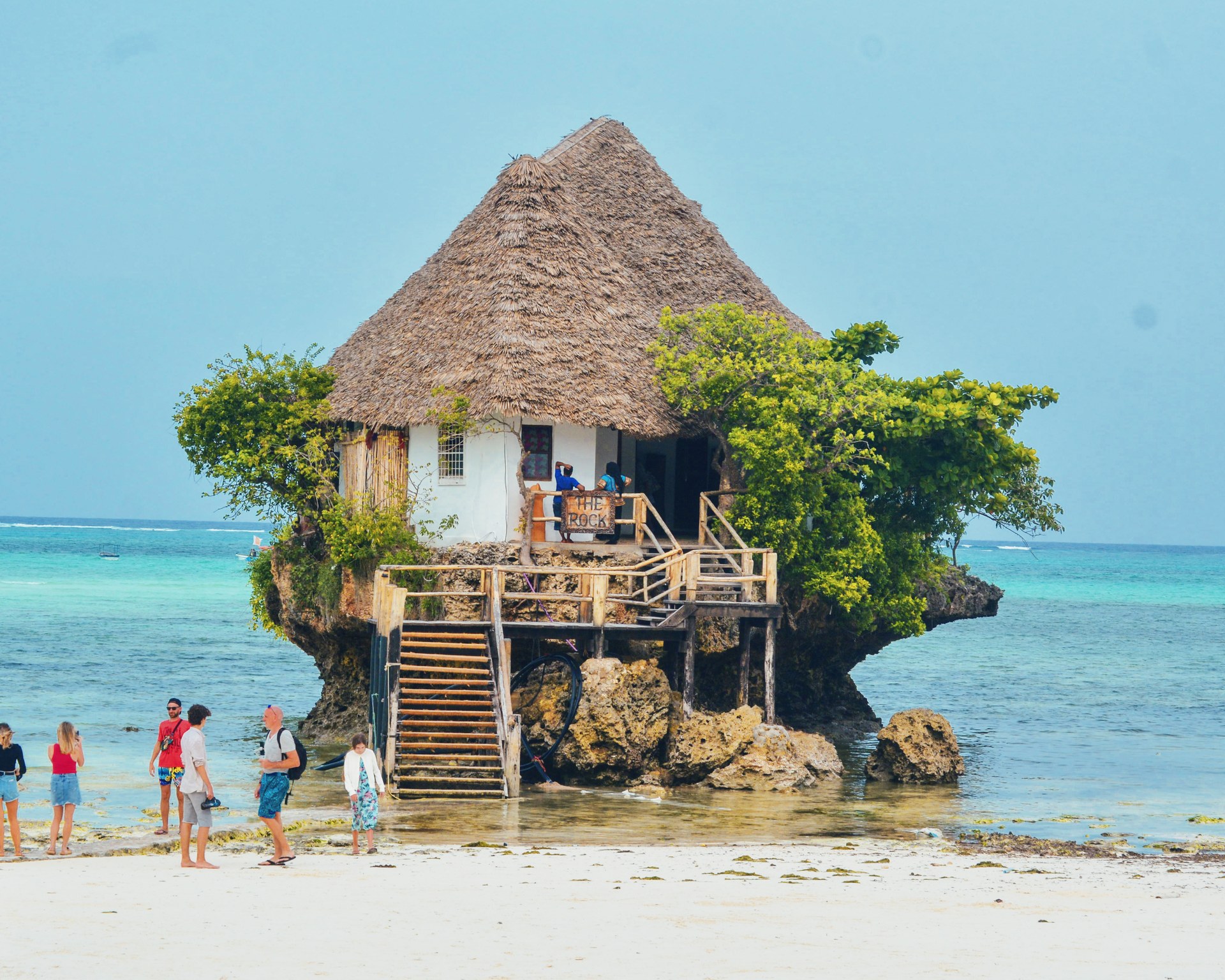 A small thatched restaurant perched on a coral outcrop standing alone in shallow turquoise water off the Michamvi peninsula, reached by a flight of wooden steps from the beach.
